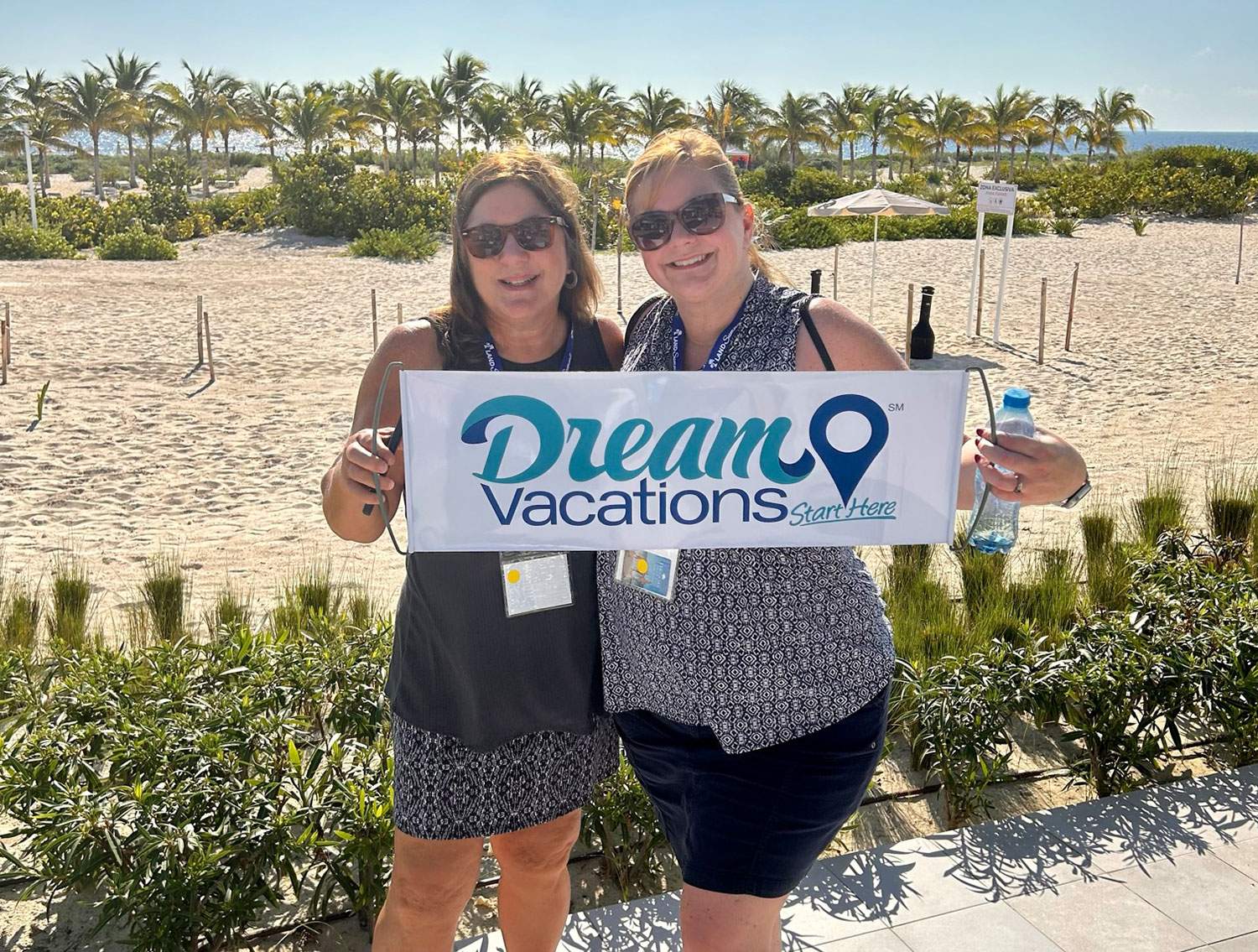 two women on the beach with a Dream Vacations sign