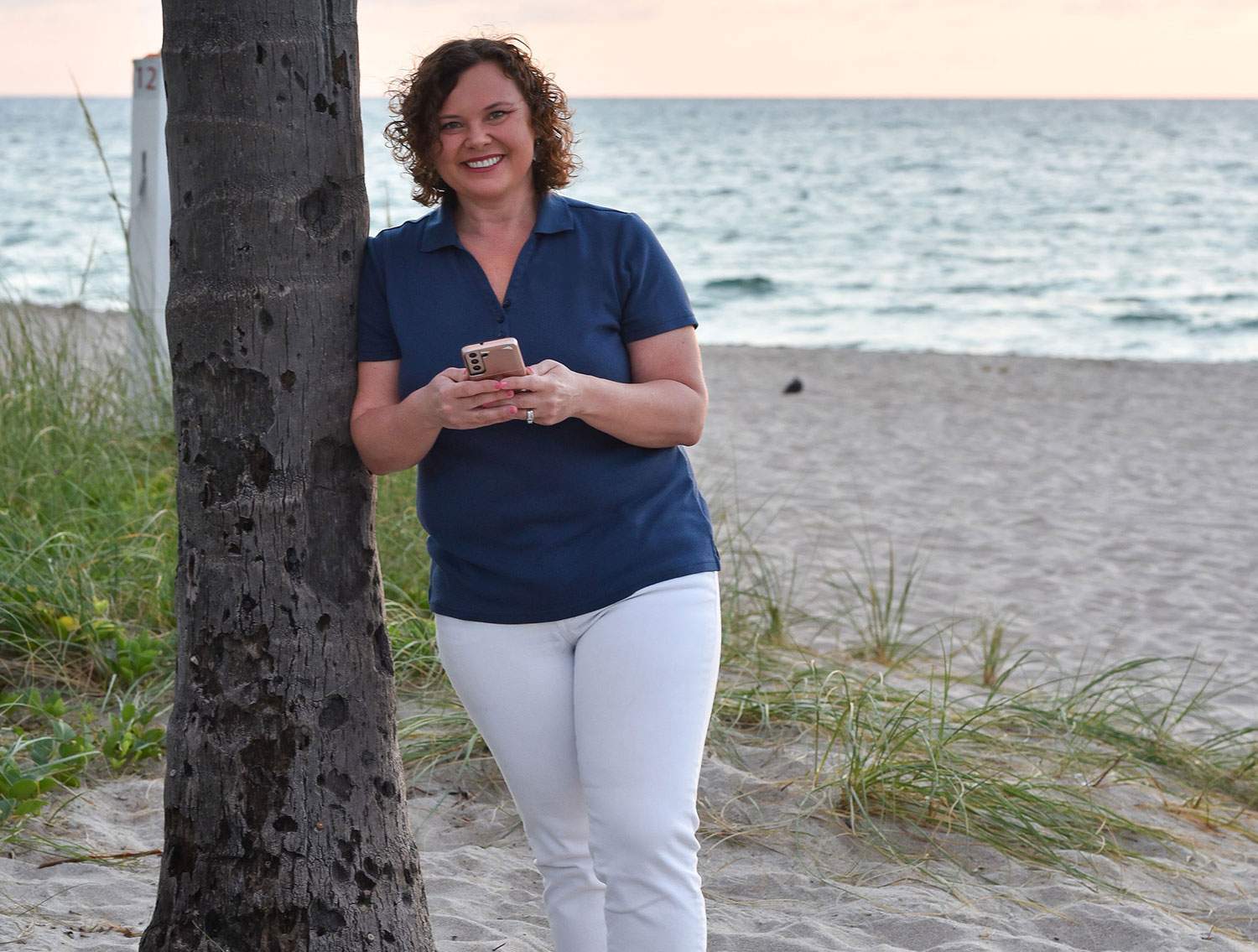 woman on the phone leaning on a tree on the sand