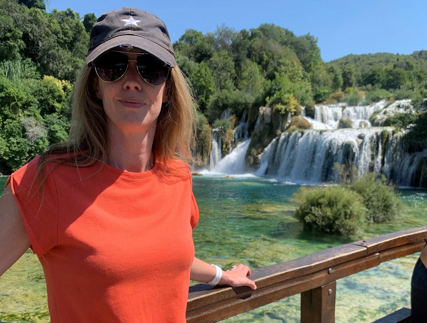 woman with hat and glasses by a waterfall